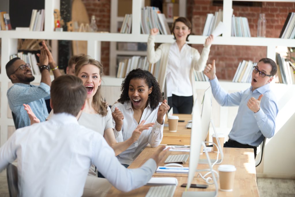 A diverse team high-fiving or celebrating in the workplace symbolizes the value of team spirit and a positive company culture