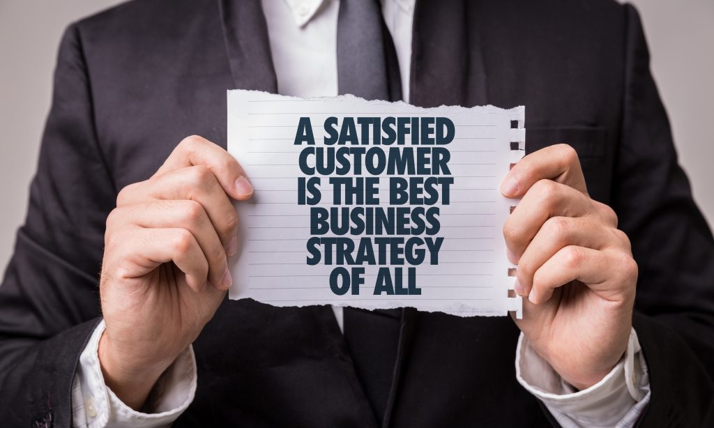 Long-term customer loyalty is illustrated by a person holding a page that says that a satisfied customer is the best business strategy of all