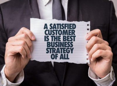 Long-term customer loyalty is illustrated by a person holding a page that says that a satisfied customer is the best business strategy of all