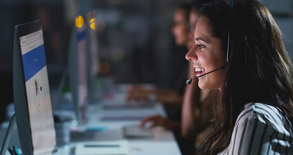 A friendly customer service agent wearing a headset and sitting in front of a computer uses fundamental soft skills in her work.