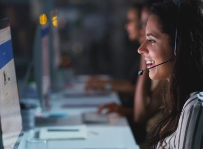 A friendly customer service agent wearing a headset and sitting in front of a computer uses fundamental soft skills in her work.